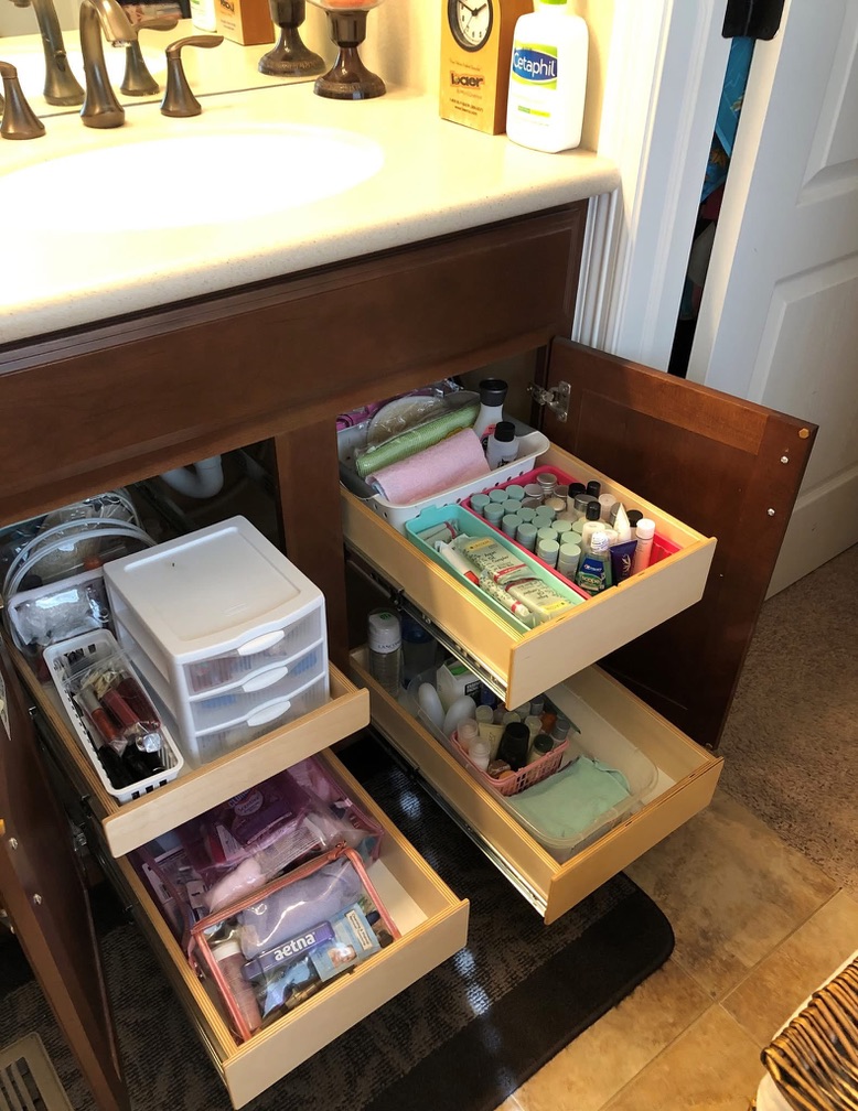 Bathroom organized An organized bathroom cabinet with open doors and three pull-out drawers neatly storing toiletries, skincare products, nail polish, and other personal care items under a sink.