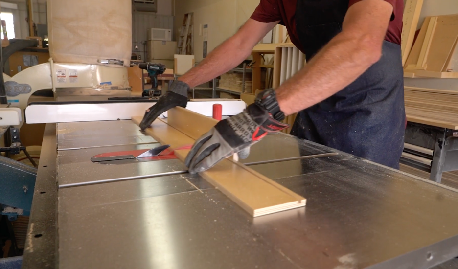 REOS workshop2 A person wearing gloves uses a table saw to cut a piece of wood in a workshop, with various tools and materials visible in the background.