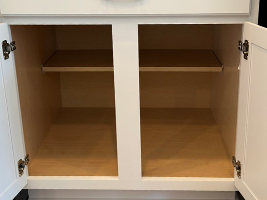 An open white cabinet with two doors, revealing two separate compartments. Each compartment has a wooden shelf, creating two levels of storage inside the empty cabinet.