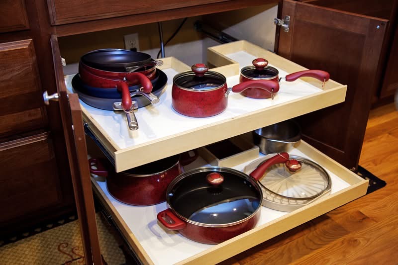 notched under stove organization A kitchen cabinet with pull-out shelves neatly holding red pots, pans, lids, and handles, organized for easy access and storage. The cabinet doors are open, showing the cookware arrangement.