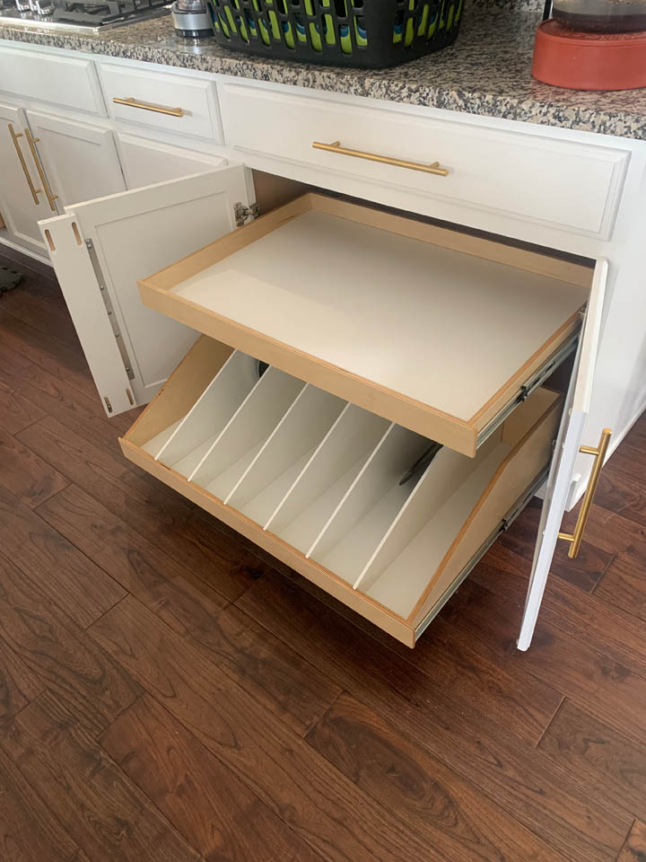 reos-product-gallery-16 A kitchen cabinet with open doors reveals two pull-out shelves: the top is flat for storage, and the bottom has vertical dividers for organizing baking sheets or trays.