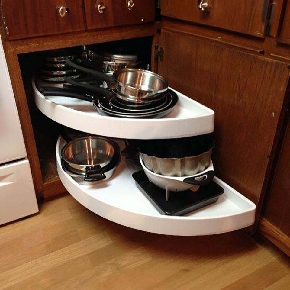 reos-product-gallery-26 A corner kitchen cabinet with two white pull-out shelves, each holding various pots, pans, and bakeware, efficiently organized for easy access. The cabinet is made of dark wood and sits on a wooden floor.