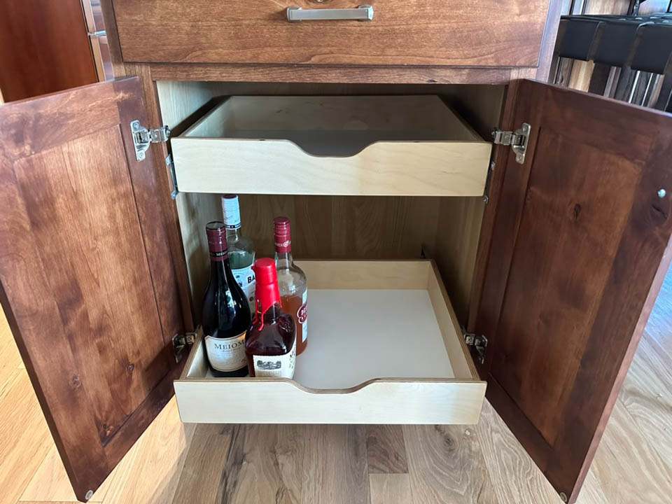 reos-product-gallery-3 A wooden cabinet with open doors reveals two drawers; the lower drawer contains various bottles of alcohol, including wine and spirits, while the upper drawer is empty.