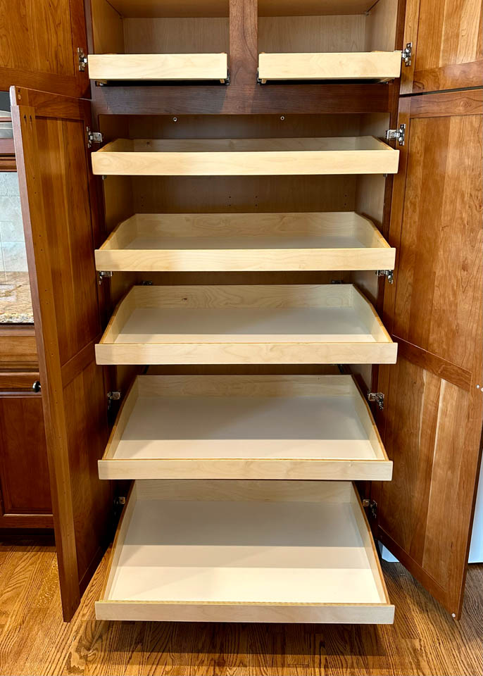 reos-product-gallery-8 A wooden cabinet with double doors is open, revealing six pull-out shelves or drawers inside. The shelves are empty, and the cabinet is set on a hardwood floor.